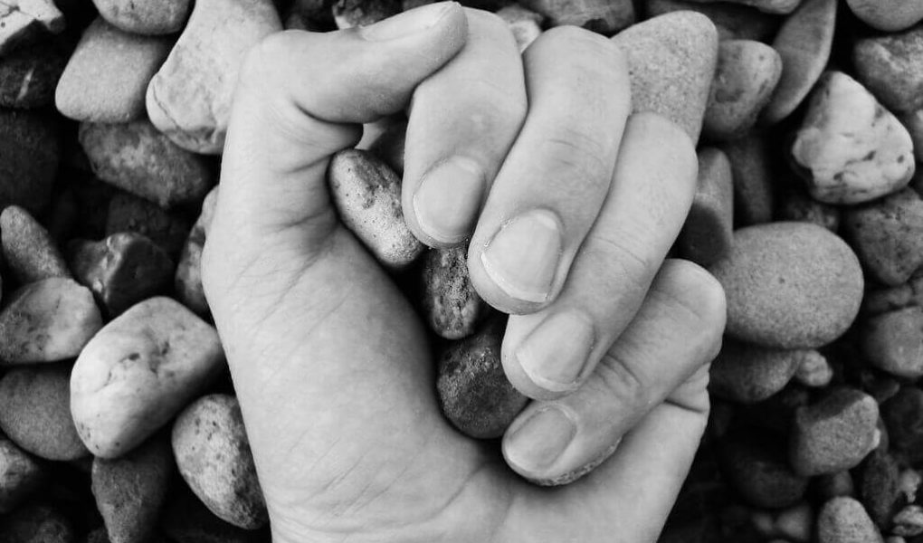 stoning, hand with stone. holding stone, with stones in the background. black and white