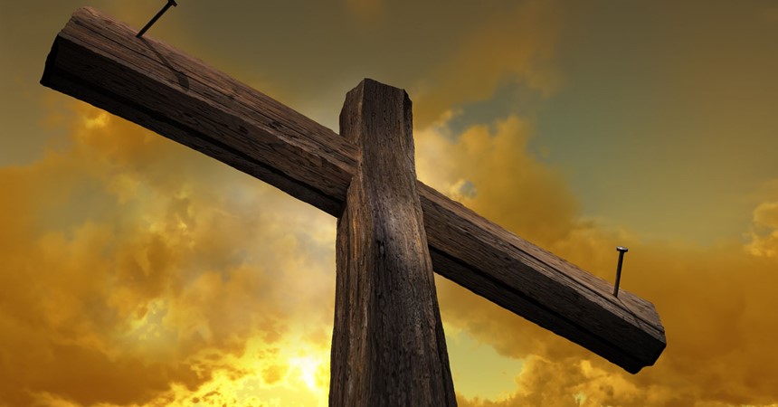 Wooden cross against the sky with shining rays at sunset and with nails